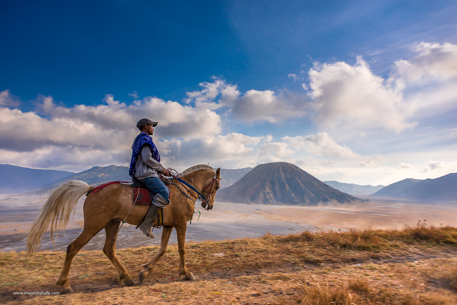 A man ridng a horse with Mount Batok in the background